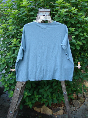Barclay Cotton Slub Cricket Cap Sleeve Tee Camo Cat Light Teal OSFA displayed on a clothes rack, showcasing its boxy shape, seamless shoulder sleeves, and rounded hemline, embodying BlueFishFinder's unique, vintage style.