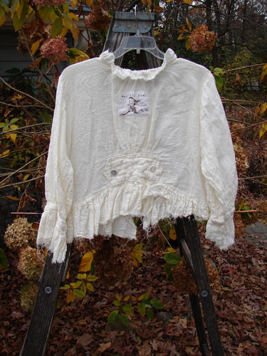 Magnolia Pearl Homespun Linen Raglan Tab Jacket Farm Love Off White OSFA displayed on a wooden swing, showcasing ruffled neckline, pearl button front, and frayed sleeve accents, embodying vintage-inspired elegance.