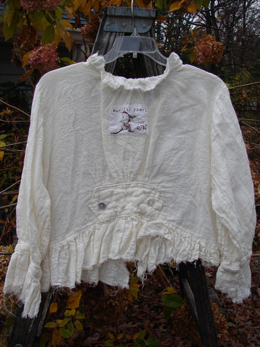 Magnolia Pearl Homespun Linen Raglan Tab Jacket Farm Love Off White OSFA displayed on a hanger, showcasing its unique ruffled neckline, frayed hemline, and embroidered MP initials for a vintage aesthetic.