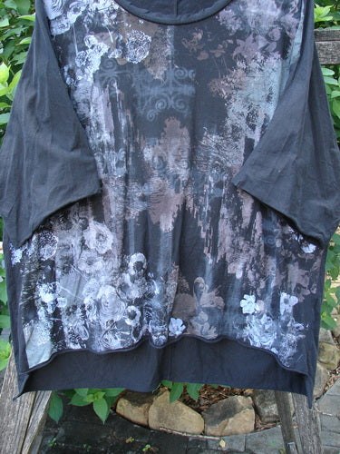 Barclay Raw Edge Flutter Collar High Low Top Dogwood Shadow Black OSFA features a floral pattern, rounded flutter neckline, short raw edge dolman sleeves, and a distinctive high-low hemline, reflecting creative individuality.