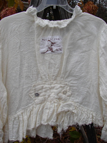 Magnolia Pearl Homespun Linen Raglan Tab Jacket with frayed sleeves, pearl buttons, and embroidered initials, showcasing unique ruffled and pintuck details, epitomizing vintage charm and individuality from Bluefishfinder.com.