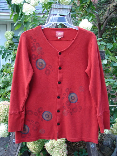 2000 Thermal Lu Top Pinwheel Bittersweet Size 2: red sweater with blue circles, ribbed cuffs, rubberized buttons, slightly A-Line shape, displayed on a swing.