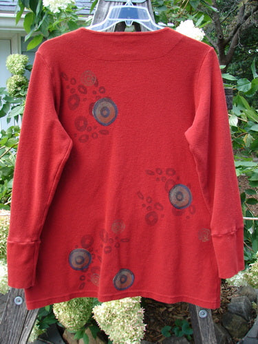 2000 Thermal Lu Top Pinwheel Bittersweet Size 2 featuring a red shirt with circular patterns, ribbed cuffs, and rubberized buttons, highlighting its slightly stretchy, lightweight, ribbed thermal fabric.