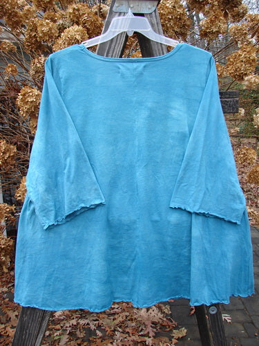 A blue shirt with sweet curly edgings on a clothes rack, part of the Barclay Three Quarter Sleeved A Lined Tee collection in mottled aqua dust, size 2.