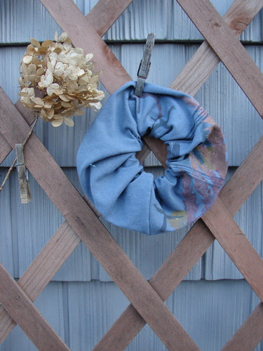 Barclay PMU Organic Cotton Hair Scrunchie Branch X Blue Dusk Extra Large, displayed draped on a wooden fence, highlighting its ruffled fabric and craftsmanship from Bluefishfinder.com's sustainable vintage collection.