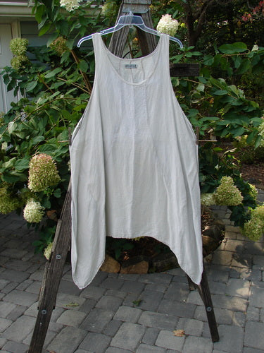 Barclay Silk Figure 8 Pinafore Unpainted Cloud Size 2, displayed on a clothes rack, showcasing unique figure-eight seams and an A-line shape with a varying hemline.