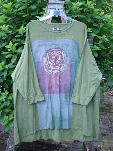 Barclay Art Tee Rose Script Mottled Peapod OSFA displayed outdoors, featuring a loose fit with three-quarter sleeves, drop shoulders, and a rounded neckline, showcasing its artistic floral design on organic cotton.