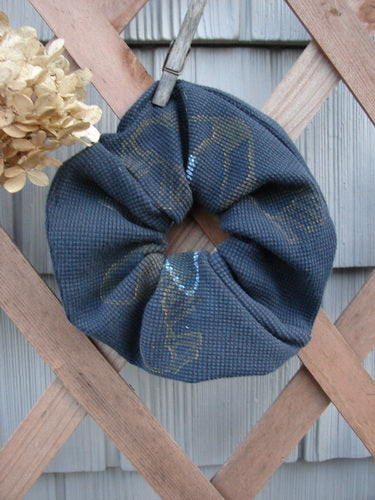 1999 PMU Thermal Hair Scrunchie Lucky Leaf Black Extra Large, showcased on a wooden fence, features ruffled fabric and elastic interior, embodying sustainable vintage design from Bluefishfinder.com.