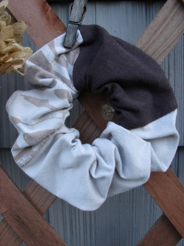 Barclay PMU Cotton & Lycra Hair Scrunchie Letter Brown Fawn Extra Large displayed on a wooden fence, showcasing its ruffled fabric and thin elastic band, embodying vintage-inspired sustainable design.