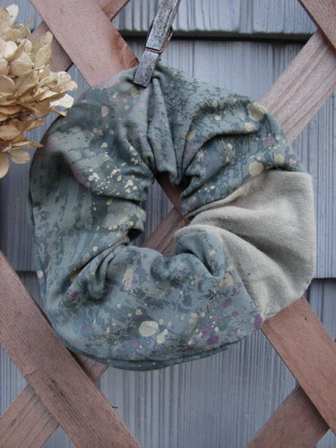 Barclay PMU Cotton & Lycra Hair Scrunchie Rain Pond Green Extra Large, featuring a ruffled fabric with paint splatter, draped on a wooden fence, highlighting its soft and forgiving texture.