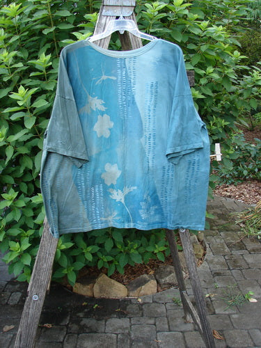 Barclay Center Seam Wide Line Tee Floral Path Mottled Turq OSFA on a wooden ladder, showcasing its wide, boxy shape, significant drop shoulders, and distinctive floral design in organic cotton.