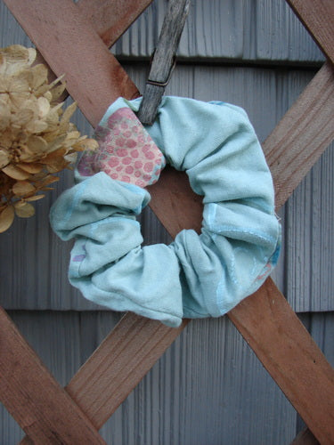 Barclay PMU Organic Cotton Button Hair Scrunchie Abstract Green Pink Medium displayed on a wooden fence, showcasing its ruffled fabric and elastic band design, emblematic of Bluefishfinder.com's vintage-inspired sustainable creations.