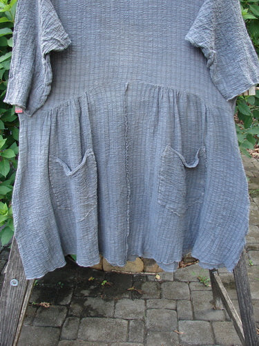 Barclay Crinkle Gauze Two Pocket Dolly Dress Mottled Slate Size 1 displayed on a chair, featuring a wide hem sweep, dual pocketed lower skirt, three-quarter sleeves, and a downward curved empire waist seam.