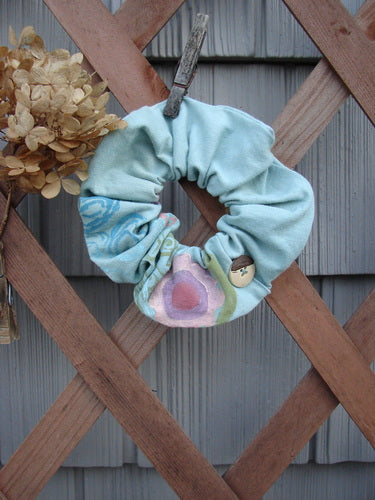 Barclay PMU Organic Cotton Button Hair Scrunchie Abstract Green Pink Large displayed on a wooden fence, showcasing its ruffled fabric and elastic band, highlighting the sustainable vintage design ethos of Bluefishfinder.com.