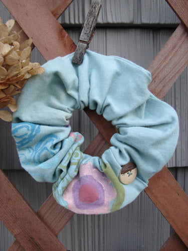 Barclay PMU Organic Cotton Button Hair Scrunchie Abstract Green Pink Large displayed on a wooden fence, showcasing its ruffled fabric and elastic interior, reflecting Bluefishfinder.com's commitment to sustainable vintage designs.