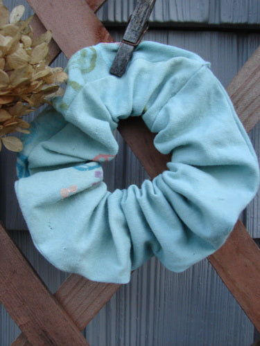 Barclay PMU Organic Cotton Button Hair Scrunchie Abstract Green Pink Large displayed on a wooden fence, showcasing its ruffled fabric and elastic band, reflecting Bluefishfinder.com's vintage-inspired sustainable design ethos.