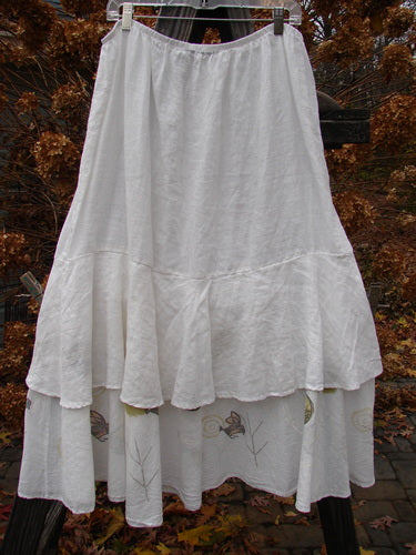 A white two-tier ruffle skirt with a floral pattern. Made from linen, it features a thin elastic waistline and a wide, flowing lower ruffle. Perfect for layering or wearing alone. Size 2.