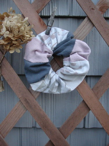 Barclay PMU Cotton & Lycra Hair Scrunchie Letter Brown Fawn Pink Extra Large displayed on a rustic wooden fence, showcasing its ruffled fabric and elastic band within a natural setting.