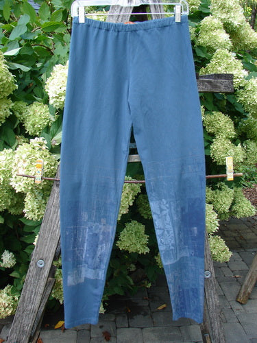 Barclay Cotton Lycra Legging Graphic Garden Echo Blue Size 1 in muted blue, with a slim stretch silhouette and smooth matte finish. The leggings hang front-facing against leafy greenery, and the lower legs show soft graphic fading in lighter blue tones.