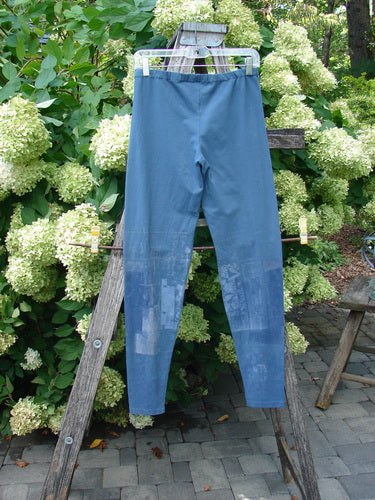 Barclay Cotton Lycra Legging Graphic Garden Echo Blue Size 1 in muted blue, with a smooth stretch knit and high-rise leggings silhouette. The pair hangs from a wooden ladder outdoors, with subtle tonal graphic patterning and soft natural light.