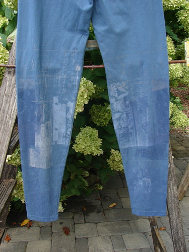 Barclay Cotton Lycra Legging Graphic Garden Echo Blue, size 1, shown in a slim blue legging cut with a soft stretch finish and faded graphic panels down the front. The pair hangs against lush greenery and stone paving, with natural light revealing the worn texture and muted denim-like tone.