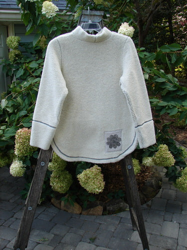 2000 PMU Fleece Pullover High Back Chair Natural Size 0 displayed on a wooden stand, showcasing a flower patch on the front, rounded hemline, and contrast stitchery.