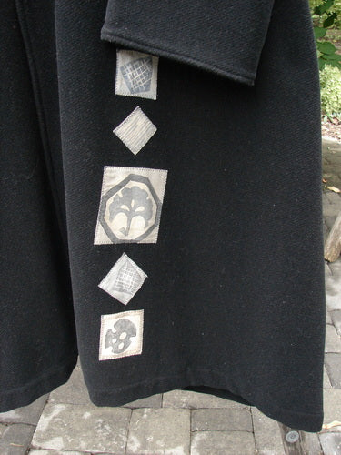 1999 Patched Woven Wool Overcoat in jet black, size 2, with a long straight silhouette and a matte wool texture. A vertical row of pale woven patch appliqués runs down the front, creating a stark graphic contrast against the dark coat.