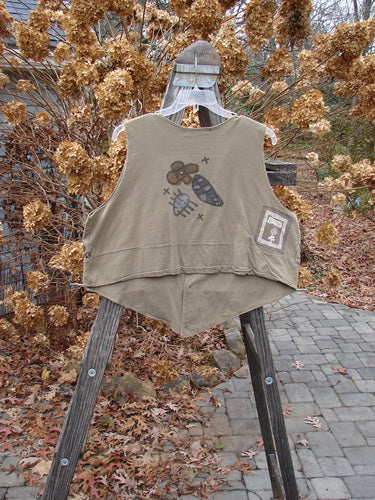 1995 Button Vest Four Petal Bramble OSFA: A vest on a wooden stand with a picture of flowers and a spider. Darling four petal and leaf theme paint, tiny front buttons, and pockets with loop closures. Crop and rounded back line, not so deep V neckline and armholes. Blue Fish patch center back.