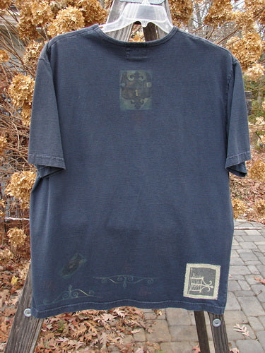 1999 Short Sleeved Tee Celtic Clock Black Size 1: Blue t-shirt with a Celtic clock theme paint and Blue Fish patch. Straight shape, rolled ribbed neckline. Made of medium weight organic cotton jersey.