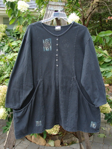 2000 PMU Patched Crepe Aran Pullover Top Celtic Knot Black Size 2 hanging on a clothesline, showcasing a blue design and decorative patches with tiny metal buttons and front exterior drop pockets.