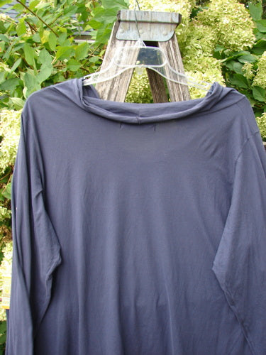 Barclay Batiste long-sleeved cowl neck layering top in unpainted royal orchid, size 2, shown as a draped navy-purple knit with a soft cowl neckline and long sleeves on a clear hanger against leafy greenery.