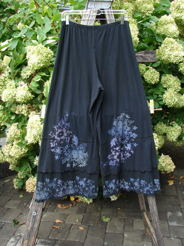 Barclay Cotton Lycra Crop Double Ruffle Pantaloon Pant Floral Black Size 1, a black cropped pantaloon pant in stretchy cotton lycra with a soft drape and double ruffle hem. Floral motifs in muted blue-gray and lavender cluster near the lower legs.