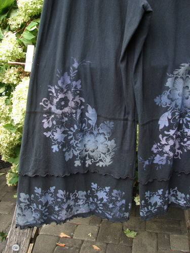 Barclay cotton lycra crop double ruffle pantaloon pant in black, size 1, with soft floral prints in muted blue-gray and lavender. The cropped legs show layered ruffle hems and a fluid knit drape, photographed close-up against greenery and paving.