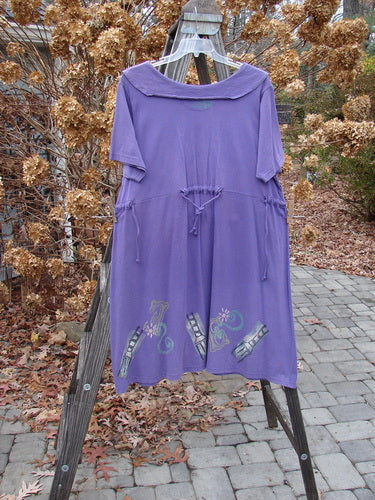 1994 Elfin Dress in Purple Nuit on Wooden Rack. Mixed 94 Theme. Framing Collar. Rear Sailor Collar. A-Line Shape. Rear Tie Tunnel. Side Ties. Empire Waist. Blue Fish Stamp. Size 2.