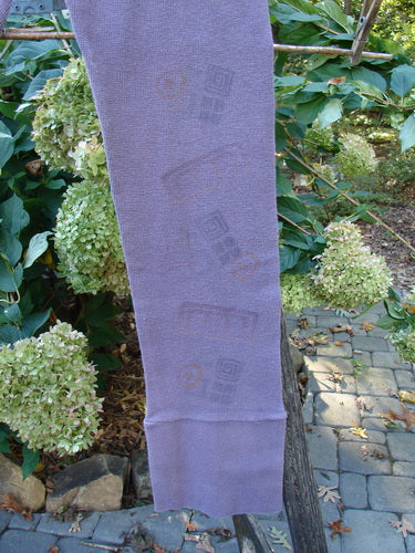 2000 Thermal Layering Lu Pant Soft Geos Eggplant Size 1 displayed outdoors, draped over a tree branch, showcasing its pocketless design and ribbed lowers, highlighting the unique geometric pattern.