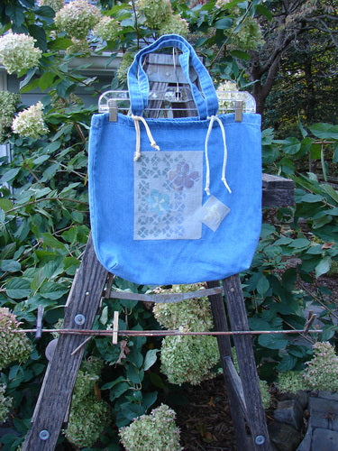 2000 PMU Cotton Tote Bag Summer Floral Washed Denim One Size on a wooden ladder, featuring colorful floral patches and tote-length shoulder straps, embodying Bluefishfinder.com's commitment to upcycled vintage fashion.