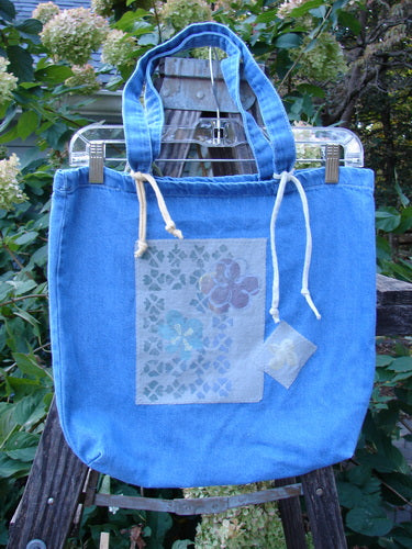 2000 PMU Cotton Tote Bag Summer Floral Washed Denim One Size displayed on a swinger, featuring tote length shoulder straps, a generous top opening, colorful rippie accents, and floral patches.