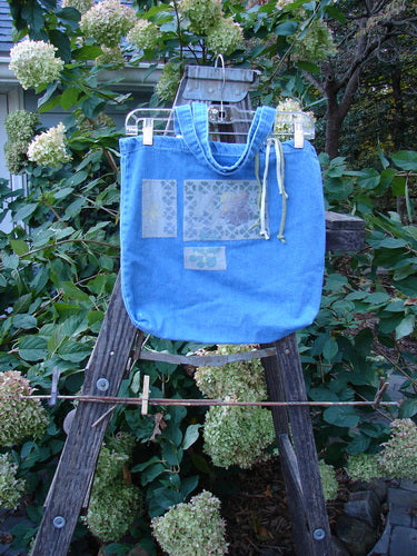 2000 PMU Cotton Tote Bag Summer Floral Washed Denim One Size positioned on a wooden ladder, showcasing tote length shoulder straps, a generous top opening, and floral patches, embodying Bluefishfinder's upcycled vintage aesthetic.