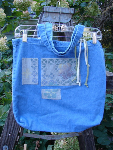 2000 PMU Cotton Tote Bag Summer Floral Washed Denim One Size displayed outdoors, featuring tote-length shoulder straps, a generous top opening, colorful patchwork accents, and a gusseted bottom for added structure.