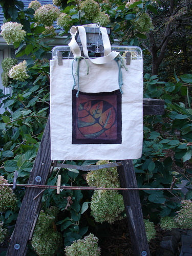 1998 PMU Patched Cotton Canvas Tote Bag Oak Leaf Natural One Size displayed on a wooden ladder, highlighting its blue straps, gusset bottom, and distinctive oak leaf patches, embodying Bluefishfinder's upcycled vintage aesthetic.