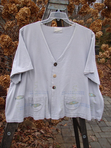 Image alt text: "1999 Tiny Pocket Top Fish Water Size 2: A white shirt with fish designs on a swinger, featuring a swingy cropped A-line shape, tiny oval bottom-shaped pockets, a deeper V neckline with a ceramic button, and the signature Blue Fish Patch. Fun fishies swim around the hemline. Bust 58, Waist 60, Hips 64, Sweep 90, Length 25 inches."