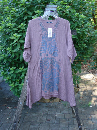 Barclay NWT Linen Venetian Dress Fern Field Tulsi Rose Size 0 displayed on a wooden rack, showcasing its oval neckline, pinched three-quarter sleeves, and varying hemline with curvy panels and tall side vents.