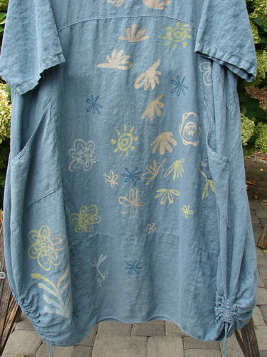 Barclay Linen Lucky Urchin Dress Floral Drift Delaware size 2 in washed blue linen, with a loose short-sleeve silhouette and scattered floral and sea-urchin motifs in pale yellow, cream, and blue. The softly textured fabric hangs in gentle folds, with gathered side seams and a relaxed, airy drape.