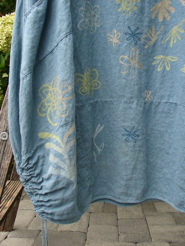 Barclay Linen Lucky Urchin Dress Floral Drift Delaware size 2 in washed blue linen, with scattered yellow and blue floral motifs, a softly gathered sleeve, and a relaxed drape that fills the frame in layered folds.