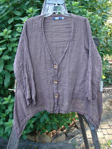 Barclay Linen Deep V Neck Three Button Top in Peat, displayed on a fence, showcasing its lightweight linen fabric, three-quarter pinched sleeves, and distinctive varying dippy sided hemline.