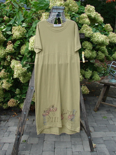 1998 Botanicals Calla Dress Echinacea Seed Size 0 in muted olive green, a relaxed short-sleeve dress with a round neckline and soft drape. Delicate botanical embroidery sits near the hem, and it is displayed on a wooden stand against leafy greenery.