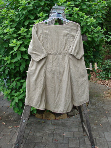 Barclay Batiste Bliss Dress Fallen Petal Stonetail Size 0 on a wooden stand, featuring a softly rounded neckline, short sleeves, two exterior pockets, and a drawcord back, showcasing its artistic petal theme.