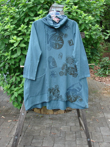 Barclay NWT Eco Cotton Cowl Pocket Tunic Star Moon Hypnea Teal Size 0 displayed on a swinger, showcasing its cowl neck and pocket detailing amidst a natural setting with leaves and greenery.