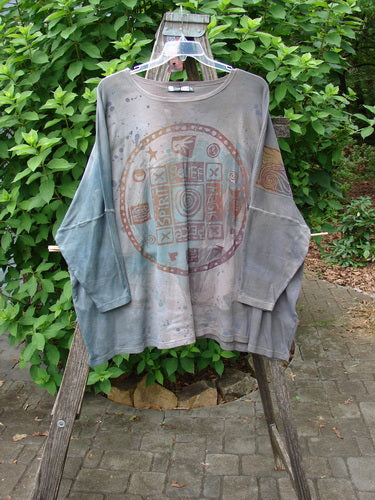 Barclay NWT Patched Supima Taos Mountain Tunic Belief Spirit Magic Peace Grey OSFA displayed on a hanger, showcasing its unique patchwork design and relaxed fit against an outdoor leafy backdrop.