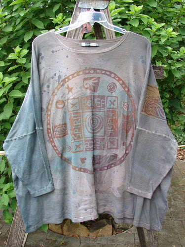 Barclay NWT Patched Supima Taos Mountain Tunic Belief Spirit Magic Peace Grey OSFA displayed on a rack, featuring a long-sleeve design with a unique painted circle pattern, measuring bust, waist, hips 70, length 30 inches.